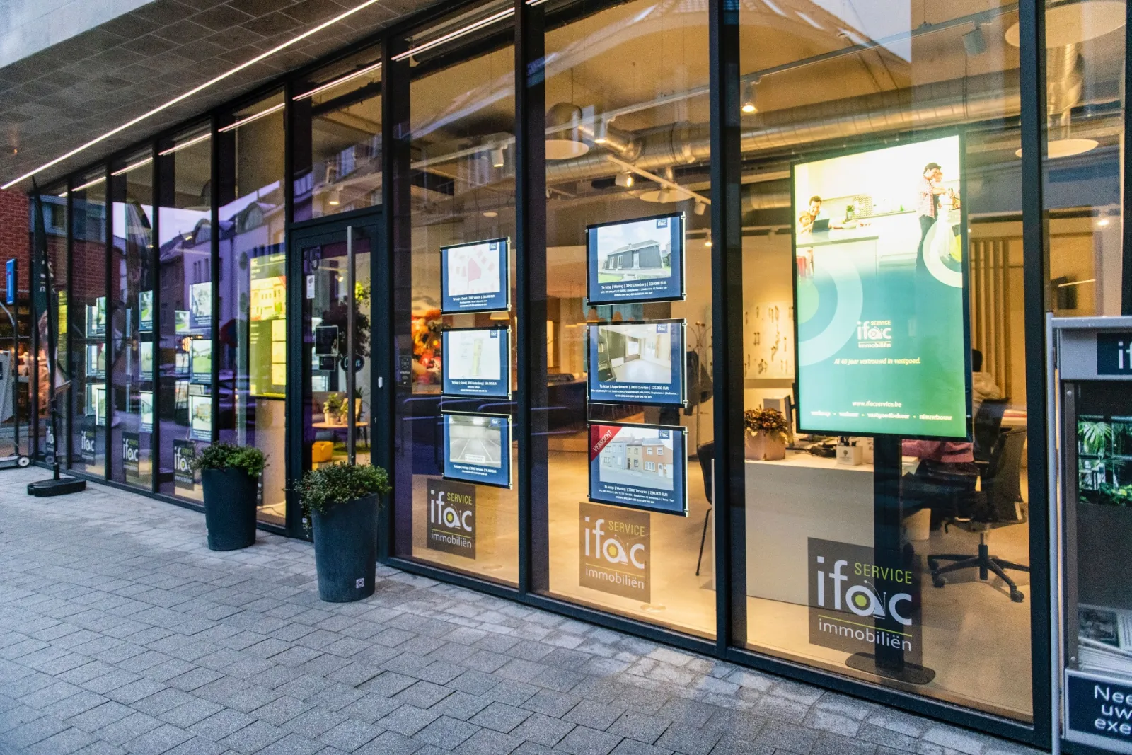De etalage van Ifac Service 's avonds, met een staand scherm en verlichte panden