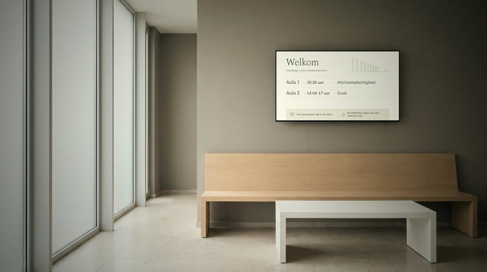 Rustige inkomhal met matglazen ramen, een lange bank in licht eikenhout en een scherm boven de bank dat welkom heet en de plechtigheden van vandaag toont