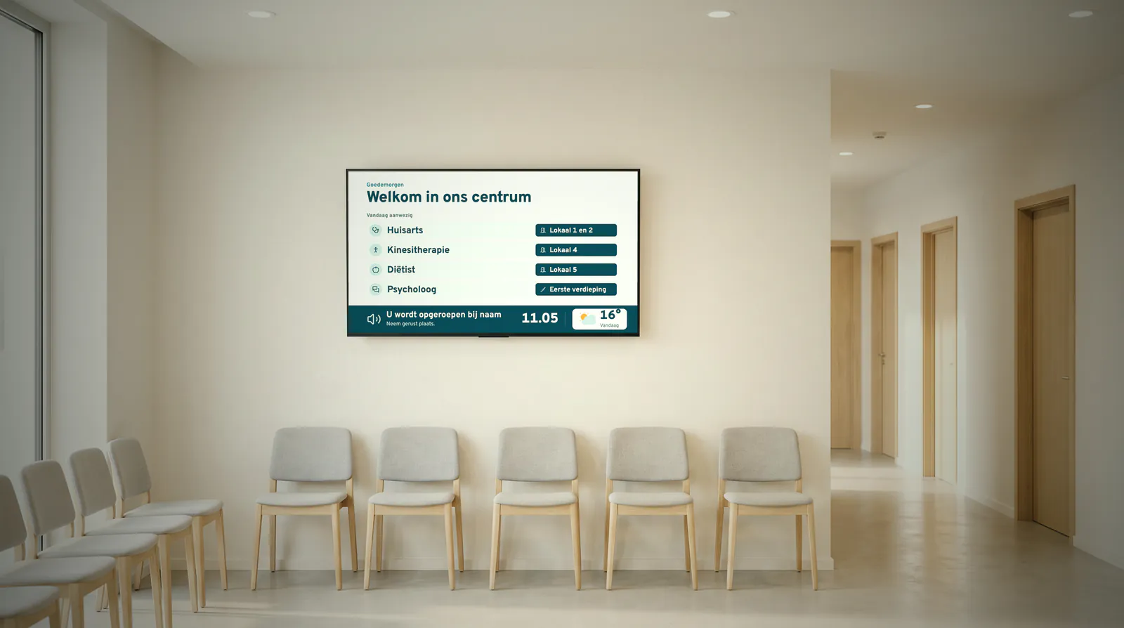 Lichte wachtzaal van een groepspraktijk met grijze stoelen langs de muur, een gang met deuren naar de behandelkamers en een scherm dat toont wie er vandaag aanwezig is